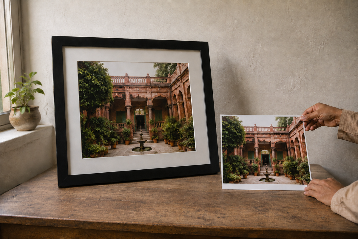 A framed photograph and matching loose print of a red-brick Lahore courtyard on a wooden table